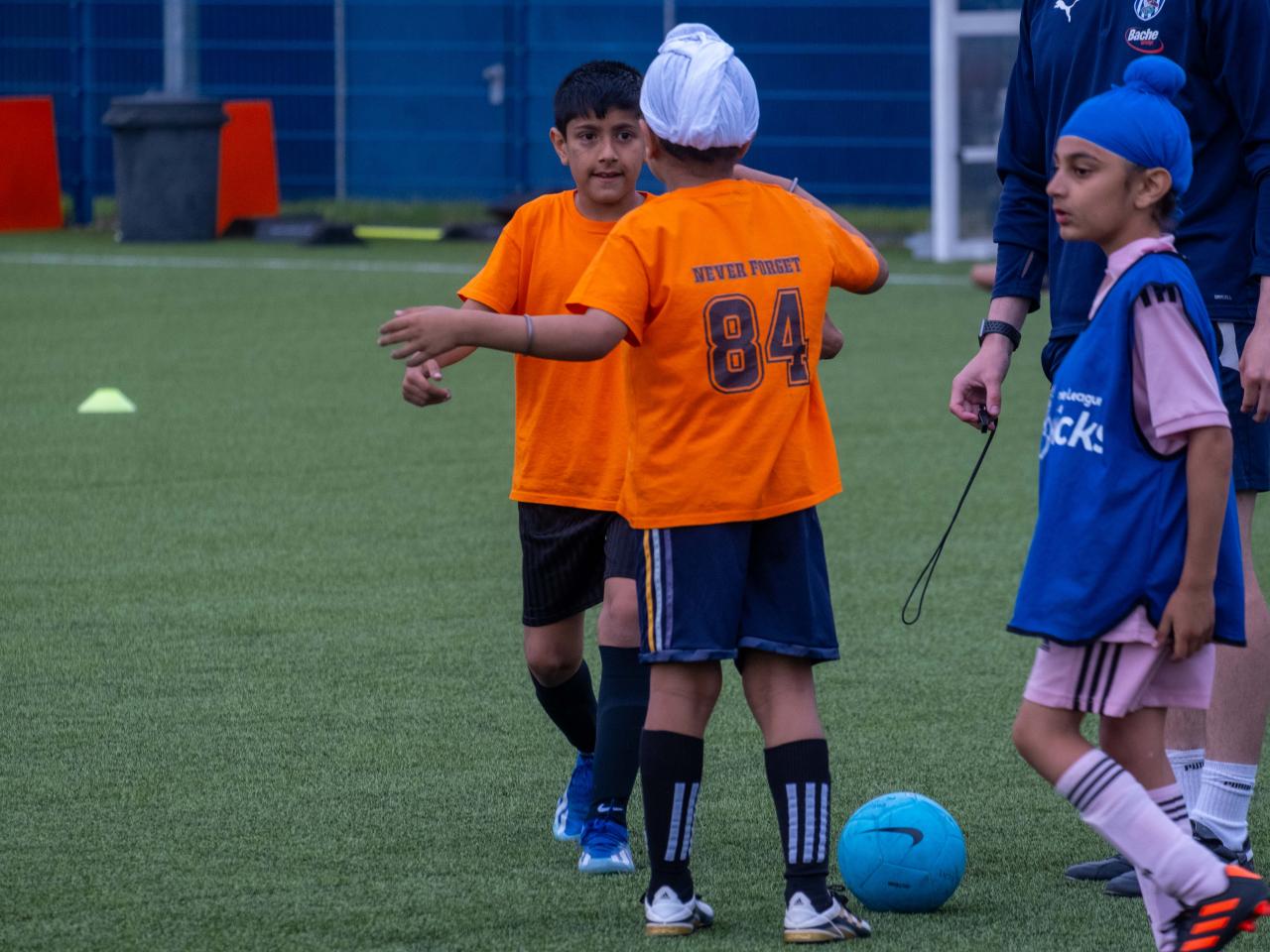 Players wearing orange shirts go to hug each other during the South Asian Emerging Talent Festival on the Academy pitch.