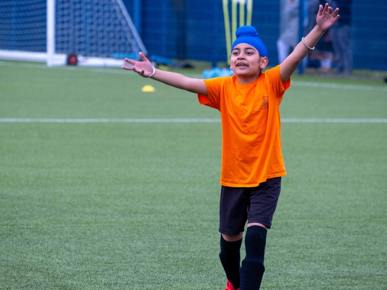 A player wearing orange holds his arms outstretched during the South Asian Emerging Talent Festival on the Academy pitch.