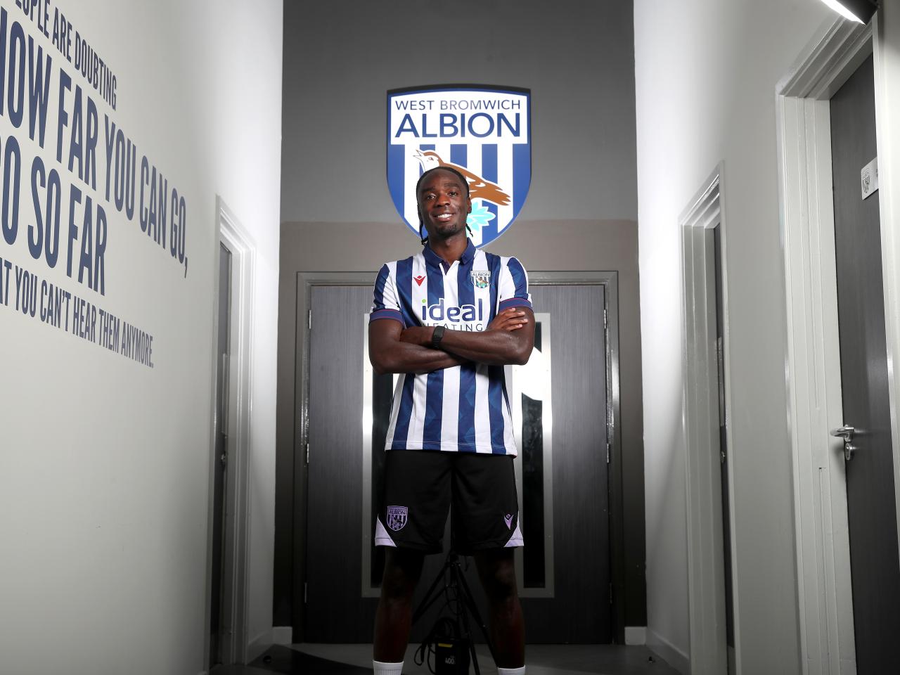Devante Cole with his arms crossed smiling at the camera wearing a home shirt 