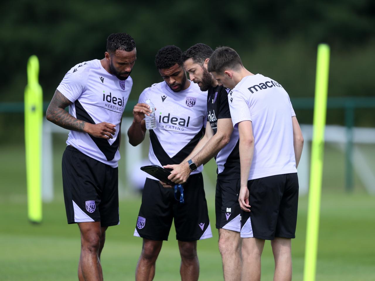 Coach Damia Abella showing information to three players on the training pitch 