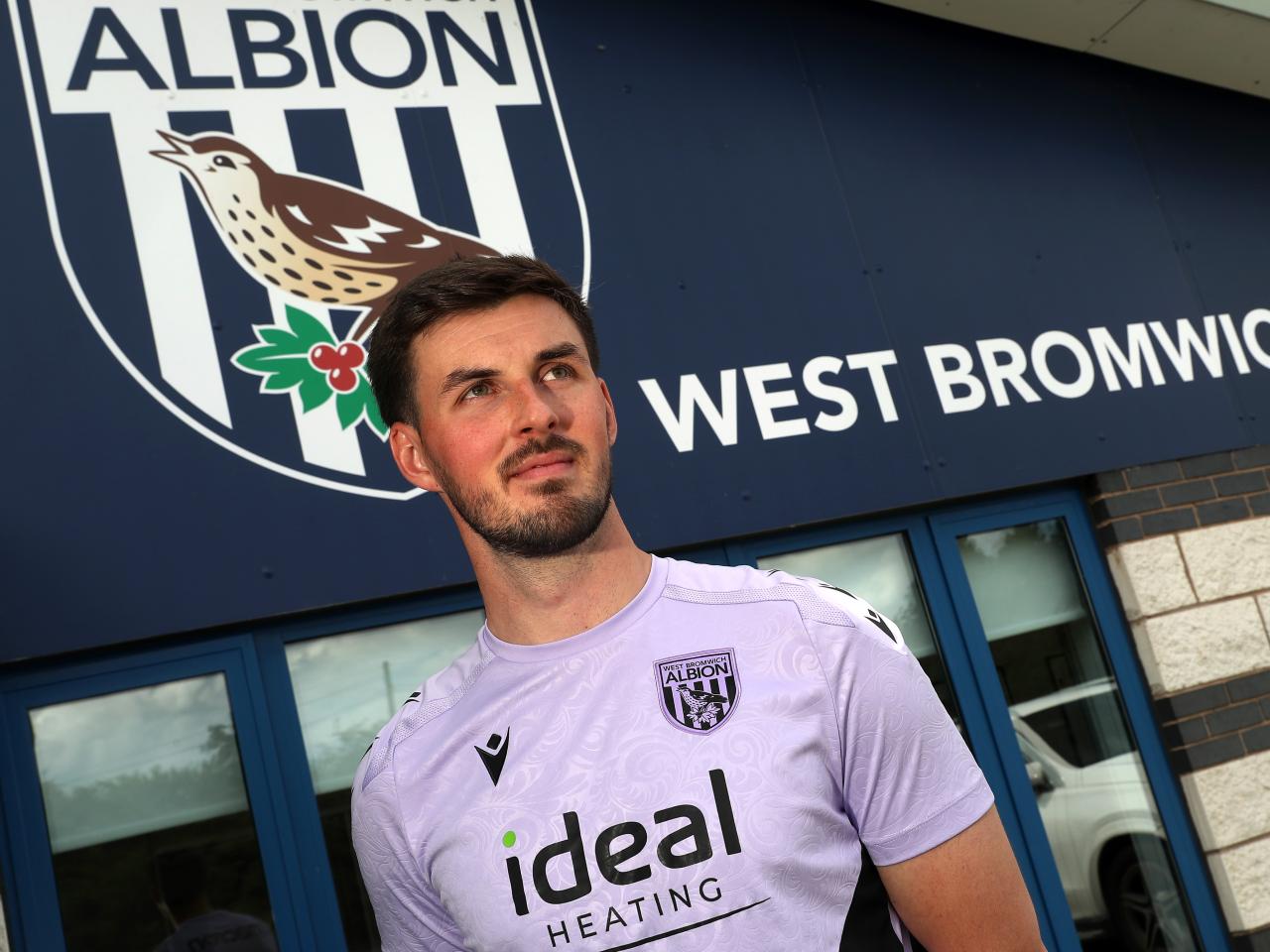 Joe Wildsmith stood in front of Albion branding at the training ground 