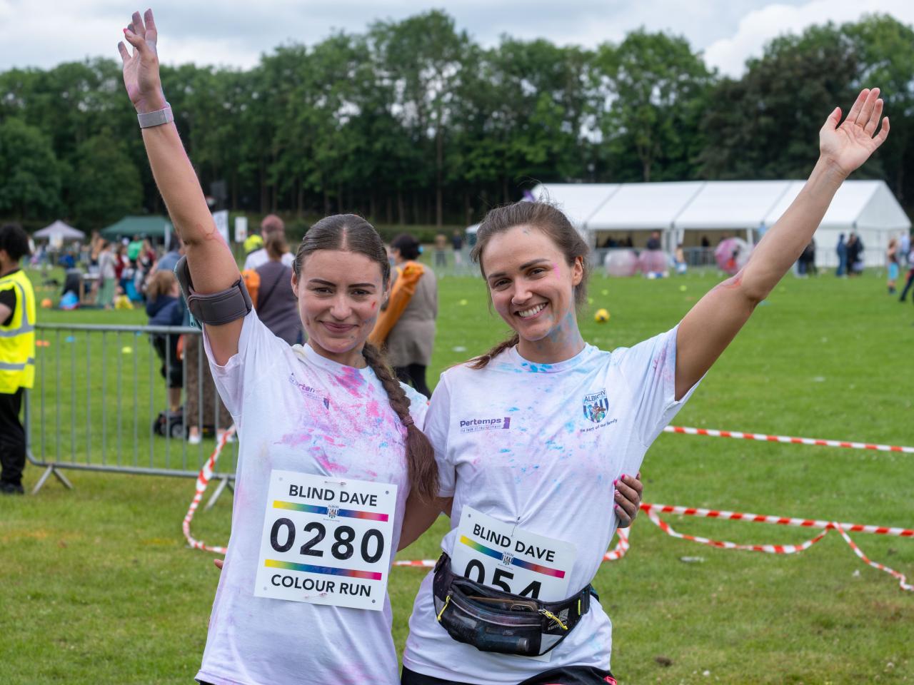 Two female participants, arms around one another and outer arms raised, pose for photo.