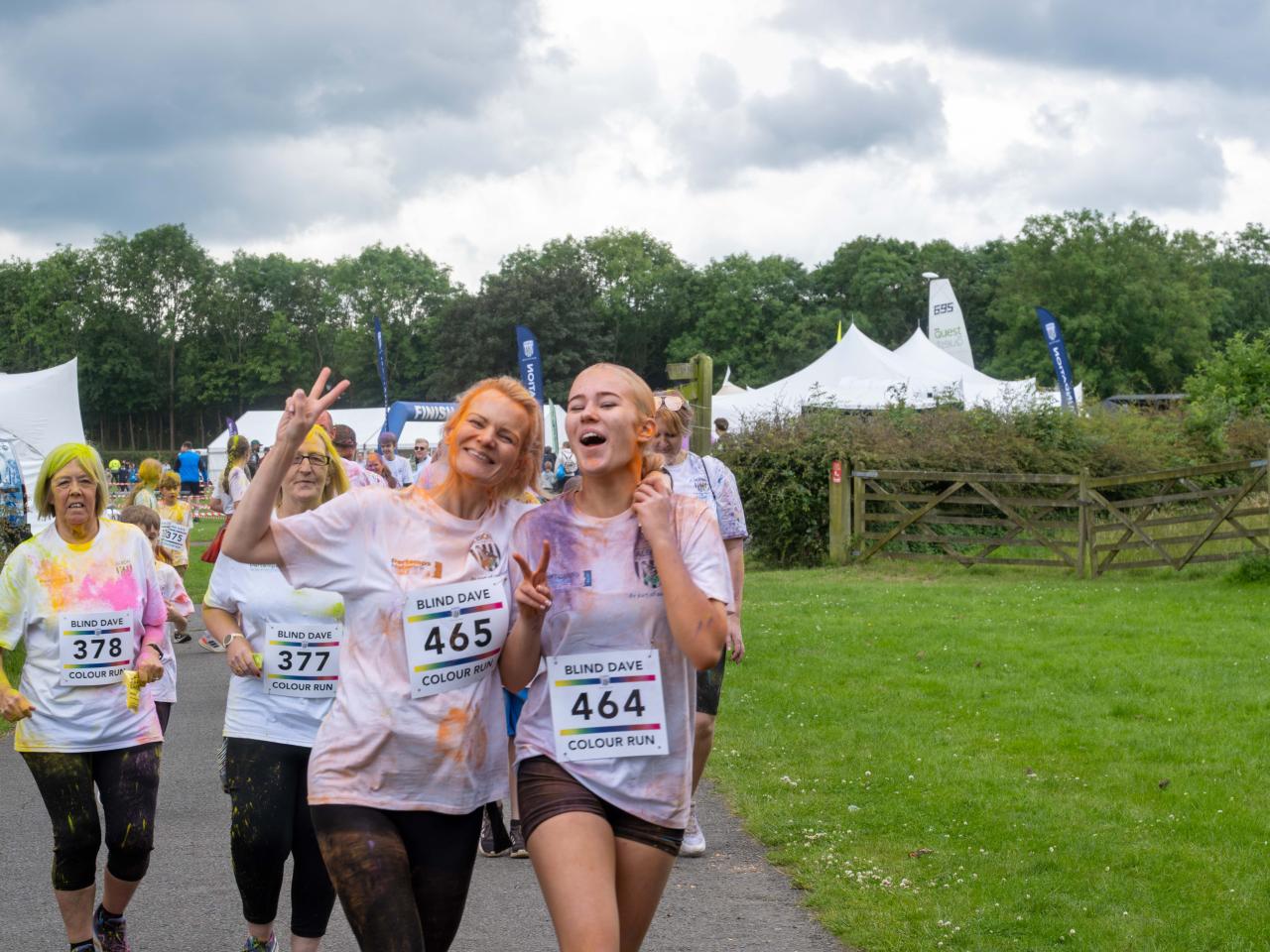 Two participants running with arms around each other. One showing peace sign, with other runners behind them.