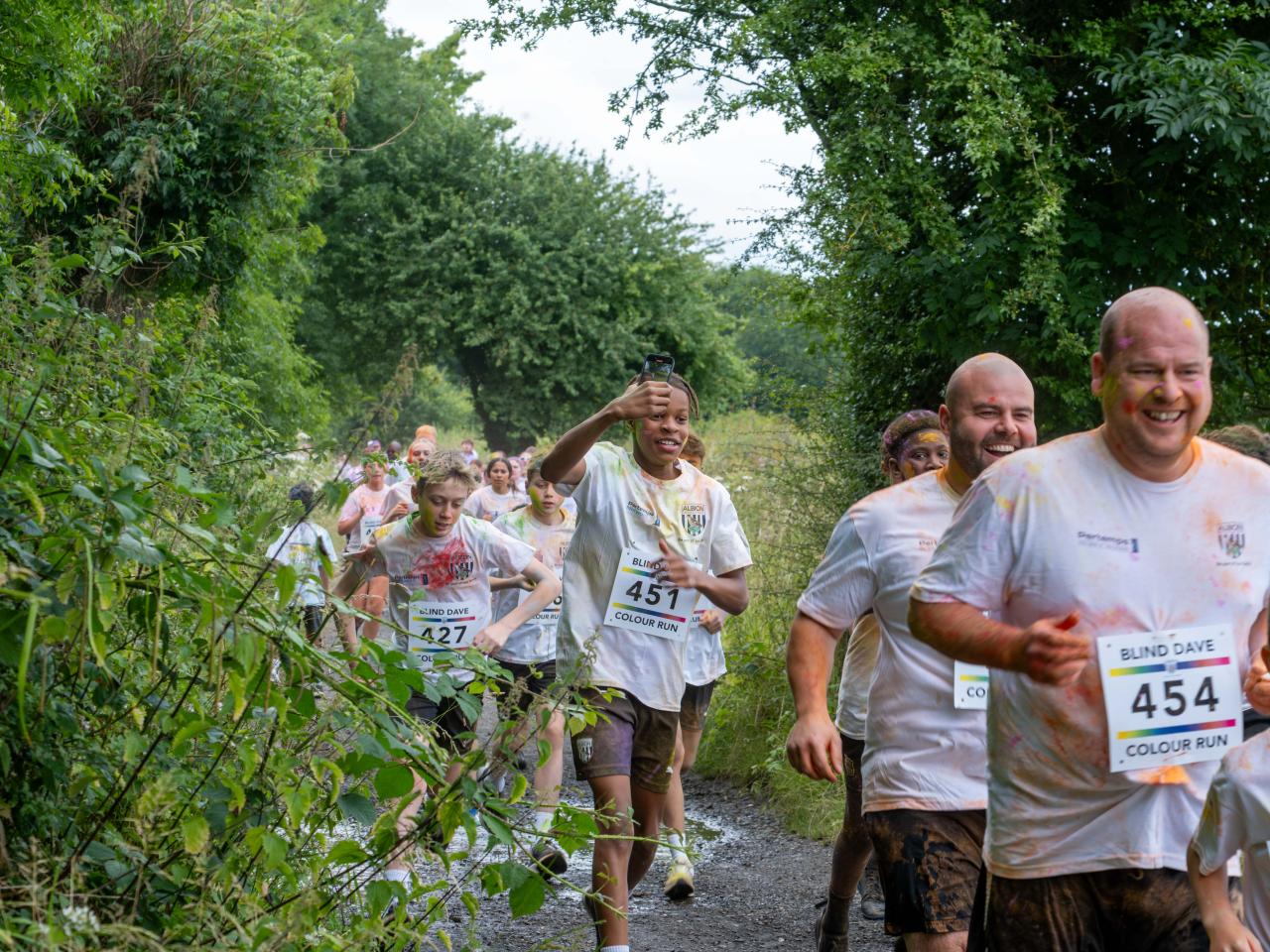 Runners heading through shrubs on Sandwell Valley Park. One participant recording on his phone.