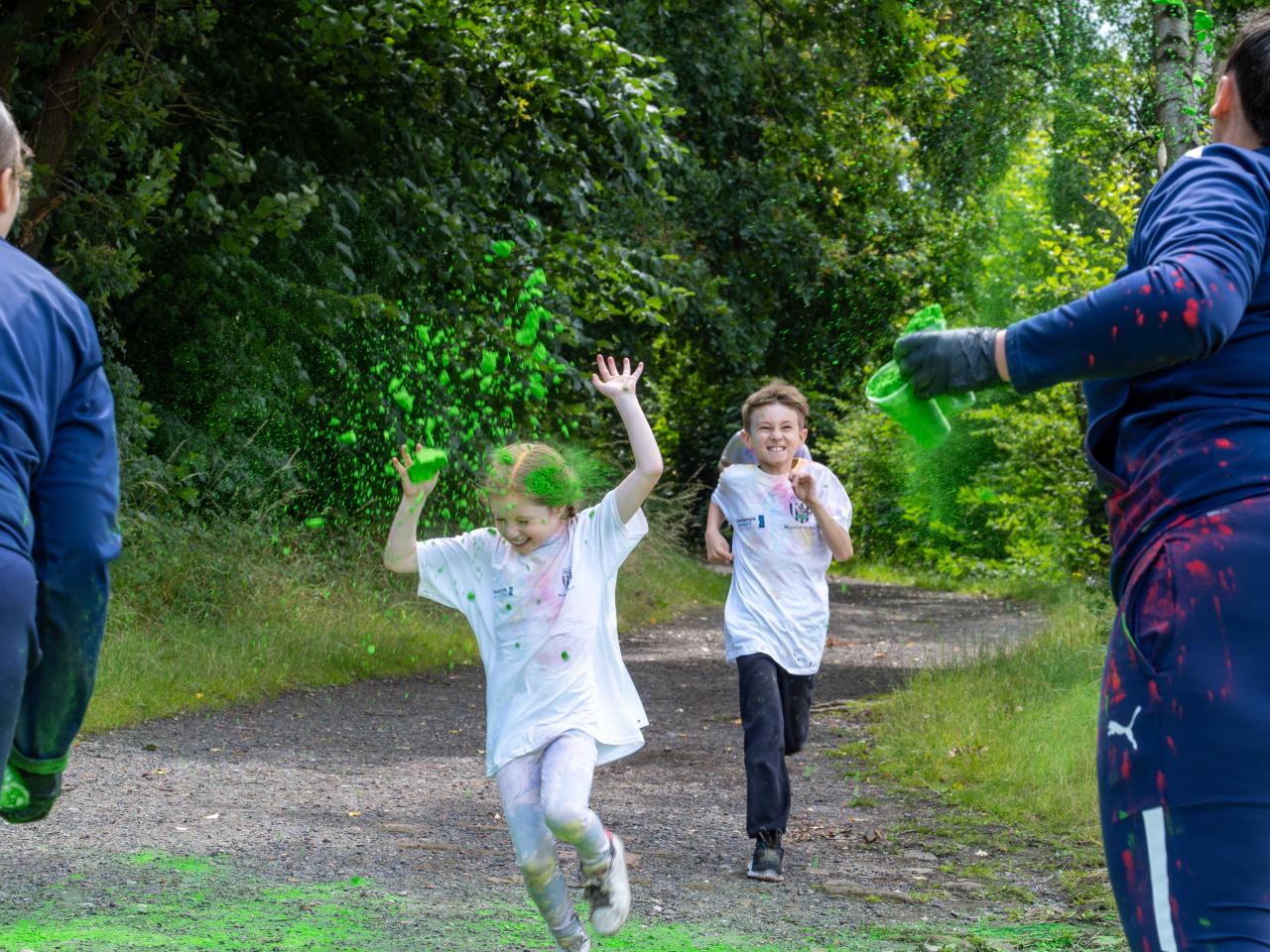 Two young participants running towards Foundation staff at a colour station, throwing paint powder.