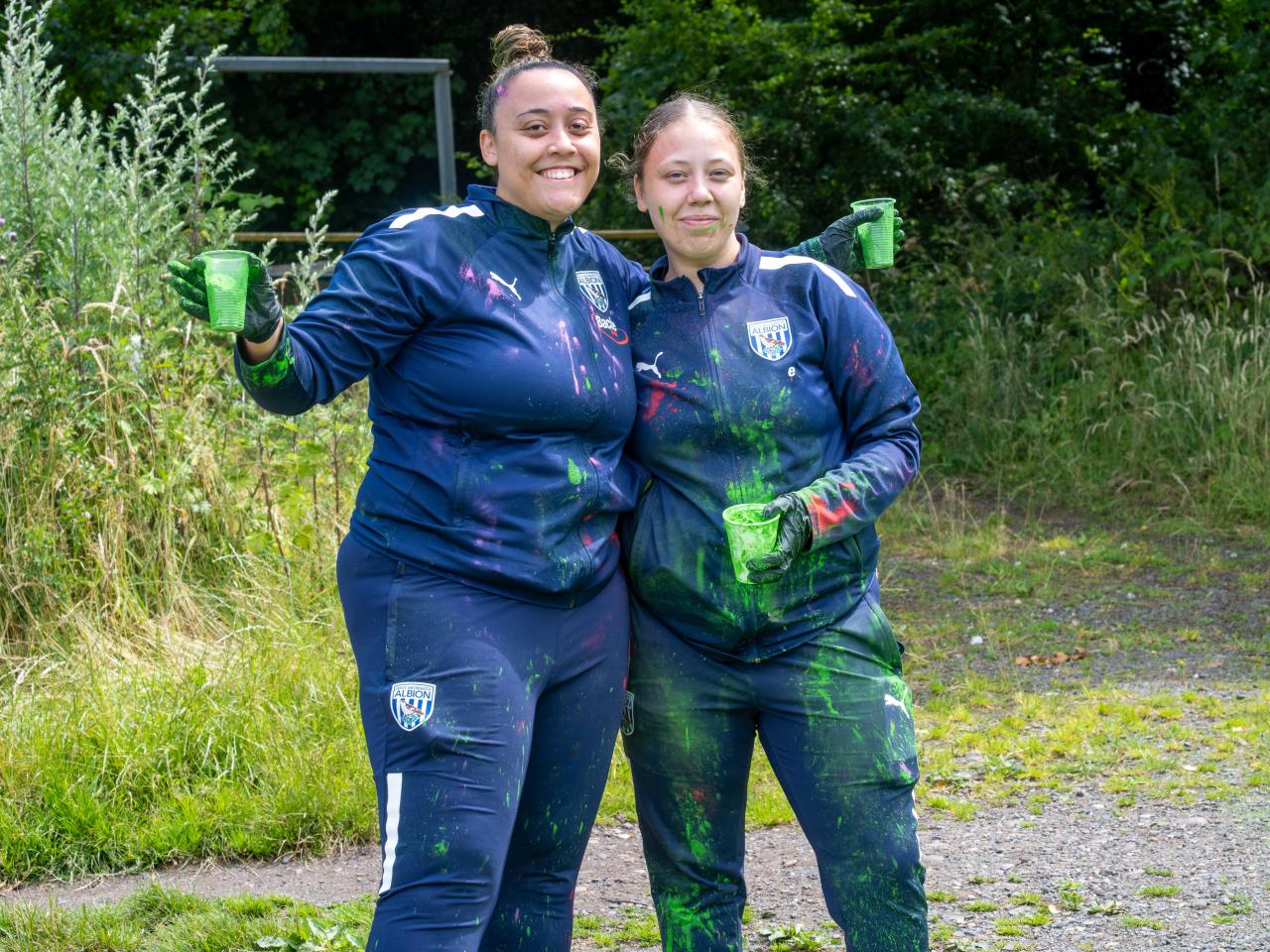 Two Foundation staff members posing for photo, holding cups of green paint powder.