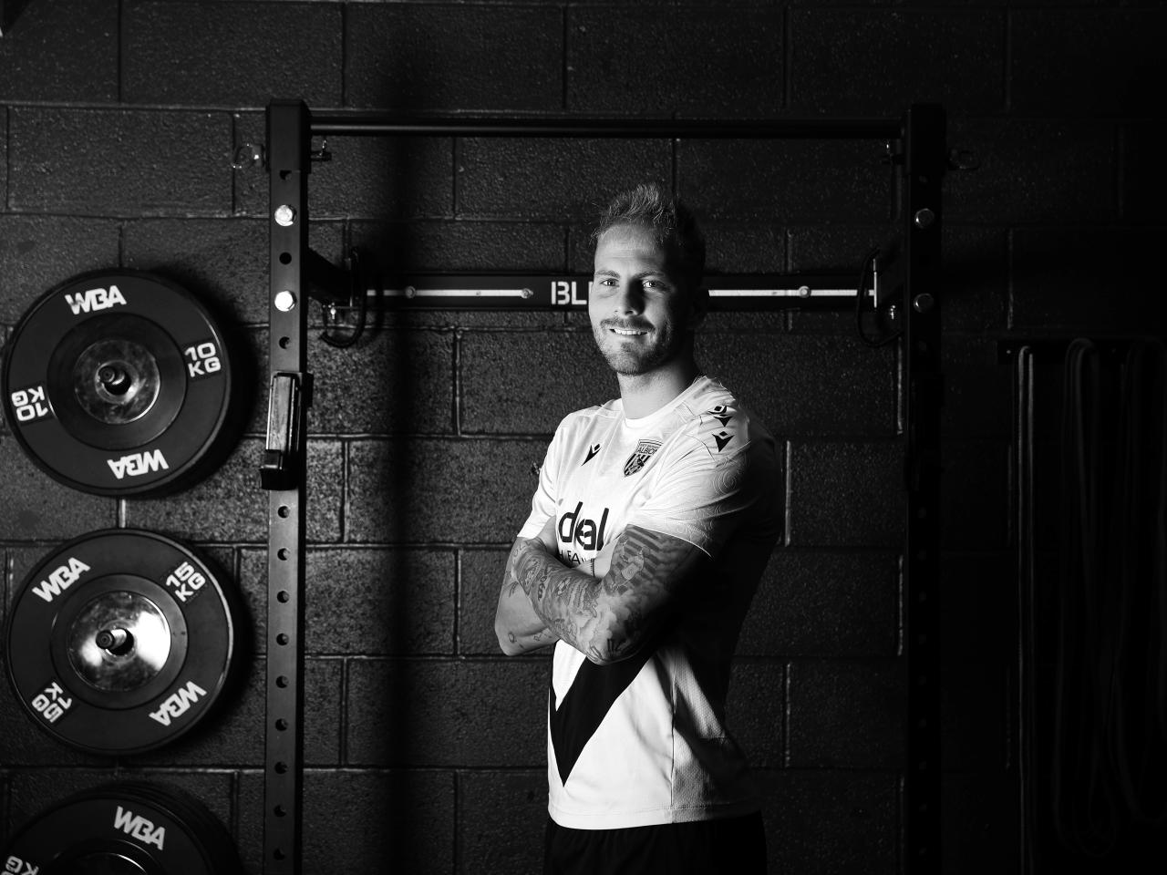 A black and white image of Uroš Račić smiling at the camera while stood in the gym