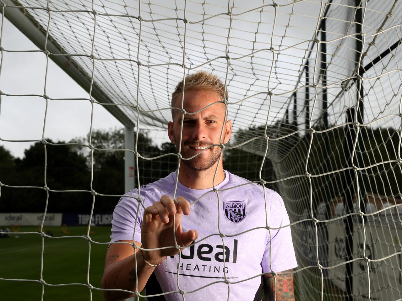 Uroš Račić smiling at the camera while looking through and holding on to a goal net 