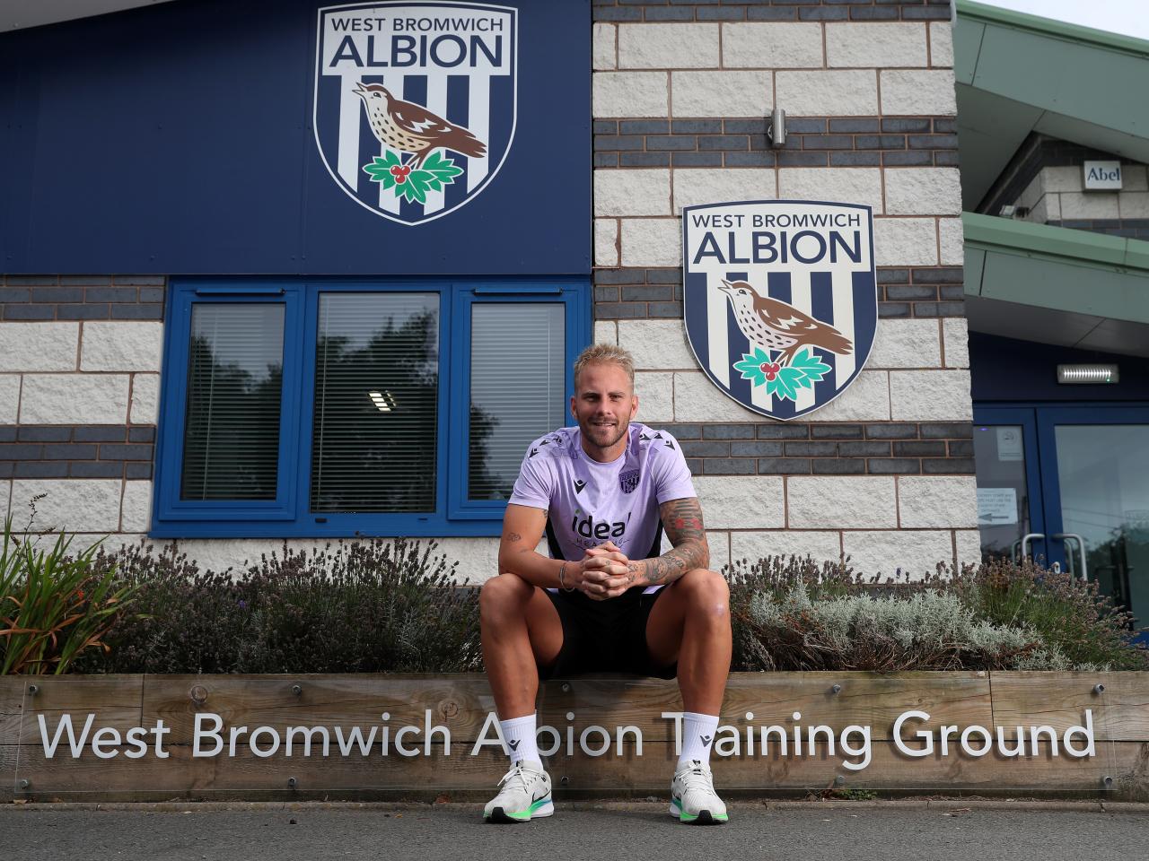 Uroš Račić smiling at the camera while sat outside the front of the training ground 