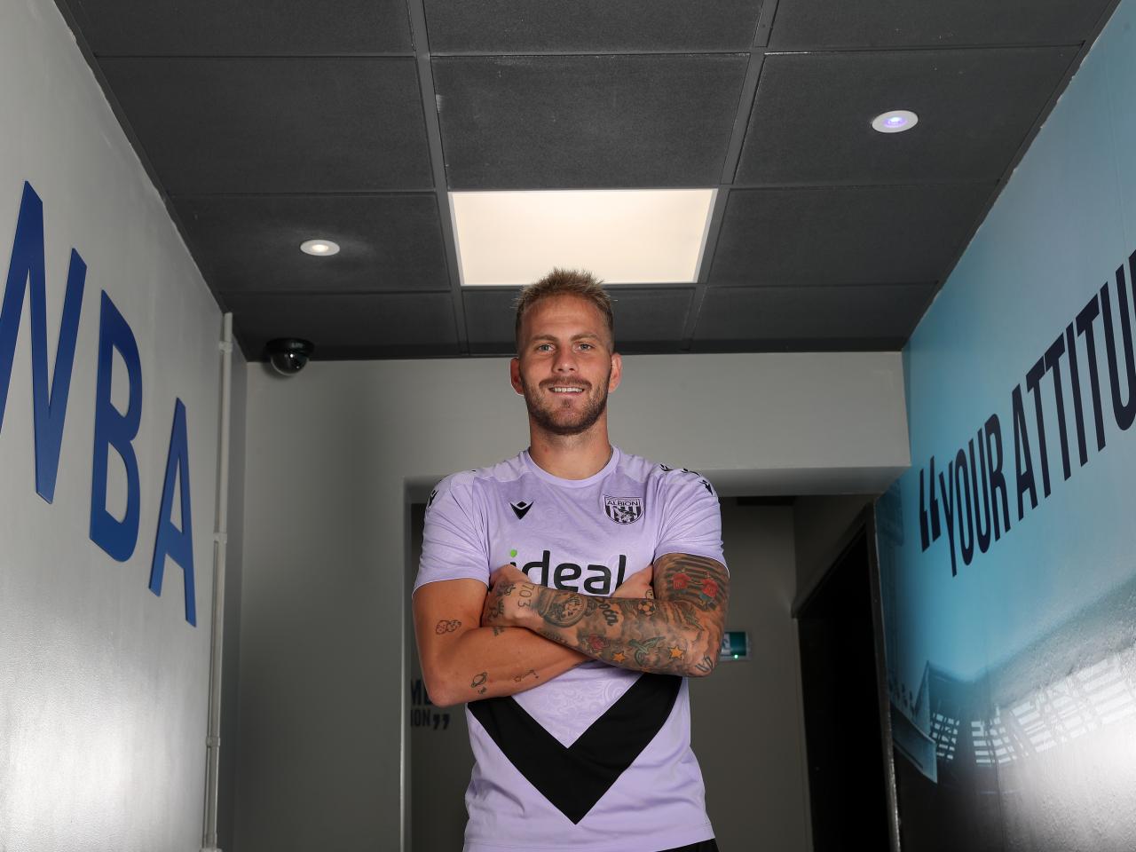 Uroš Račić smiling at the camera while stood in a corridor with his arms folded 
