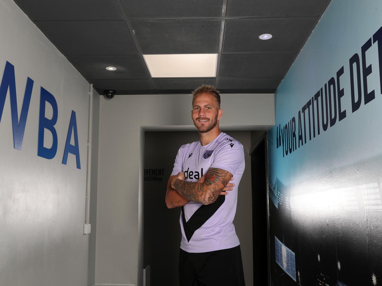 Uroš Račić smiling at the camera while stood in a corridor with his arms folded 