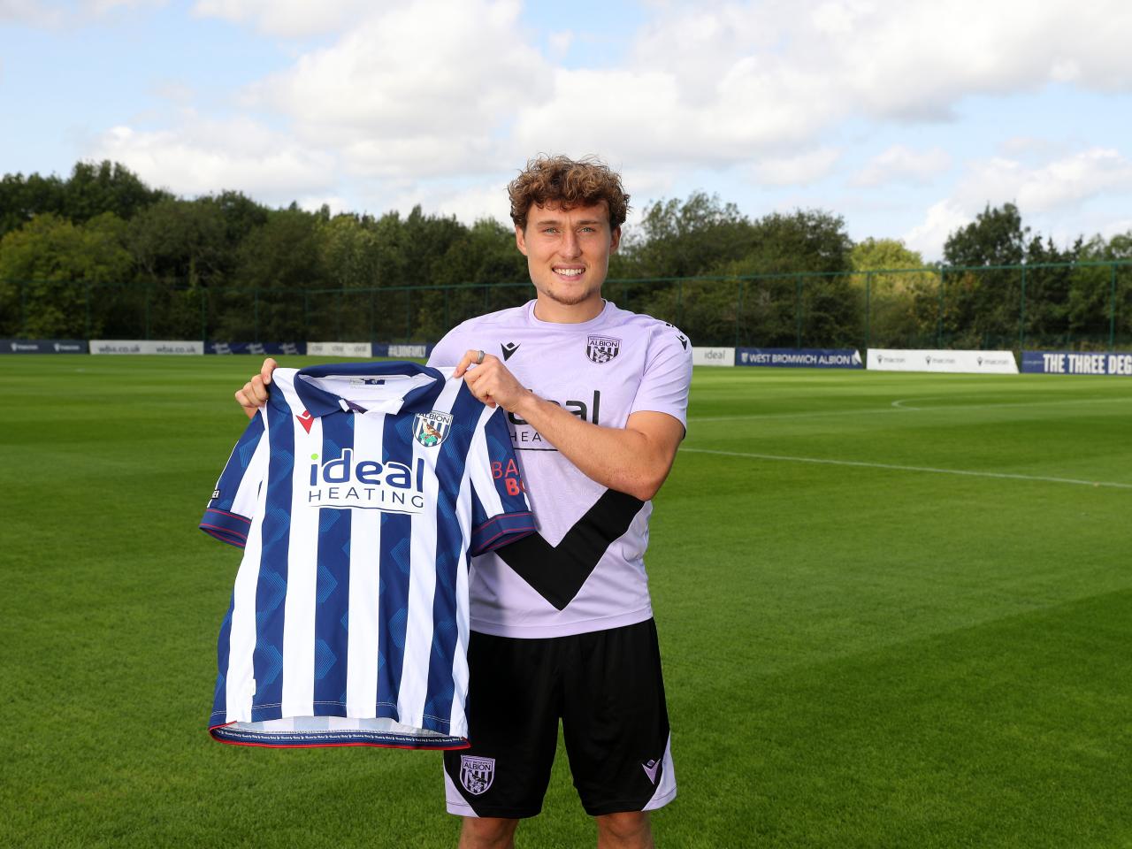 Callum Styles smiling at the camera while holding a home shirt 