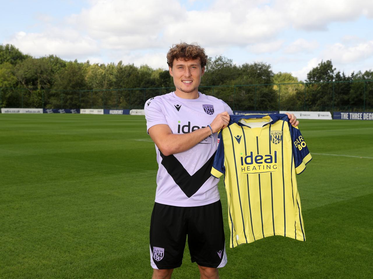 Callum Styles smiling at the camera while holding a yellow away shirt 