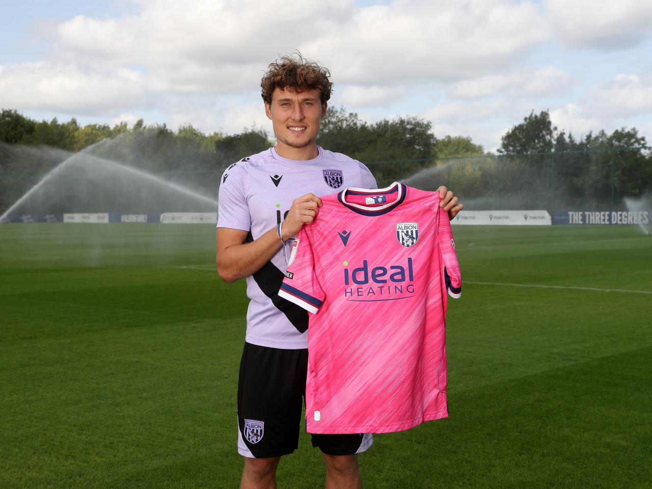 Callum Styles smiling at the camera while holding a pink away shirt 