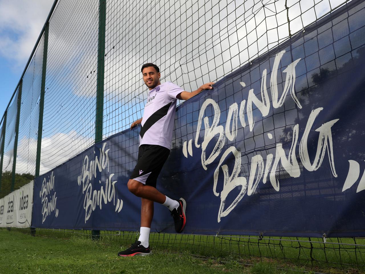 Gianluca Frabotta smiling at the camera while stood next to branding around a pitch which reads boing boing