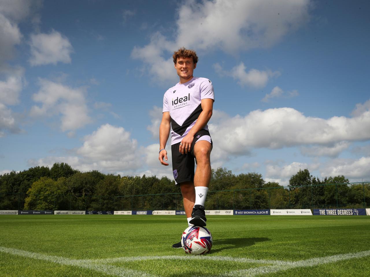 Callum Styles smiling at the camera with one foot on the ball out on the training pitch 