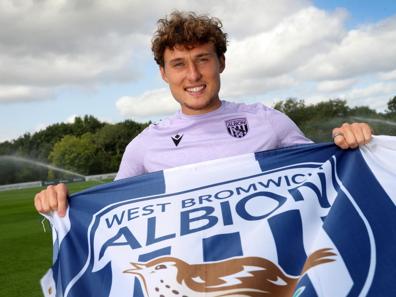 Callum Styles smiling at the camera while holding a WBA flag