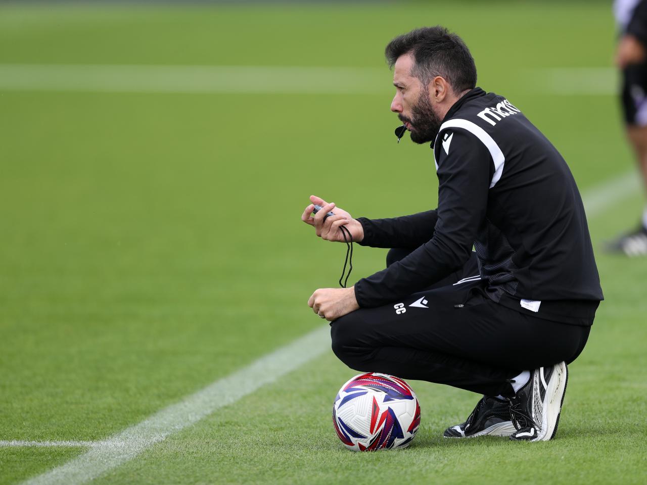 Carlos Corberán watching training crouched down with a whistle and a ball
