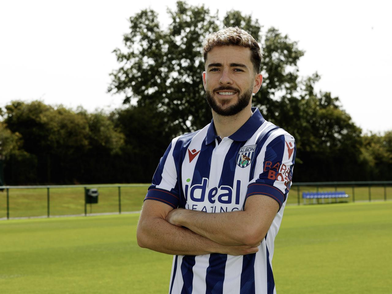 Mikey Johnston smiling at the camera while stood with his arms folded in a home shirt 