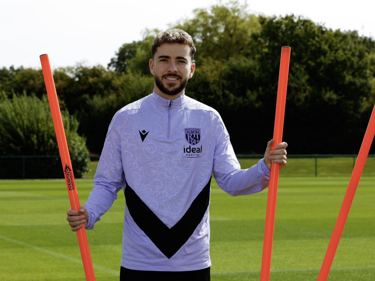 Mikey Johnston smiling at the camera while stood by some poles on the training pitch