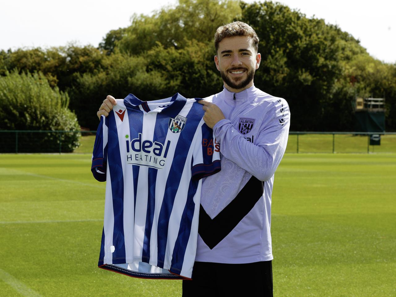 Mikey Johnston smiling at the camera holding up a home shirt 