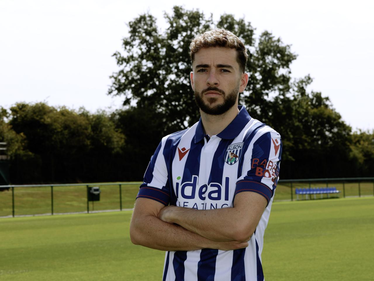 Mikey Johnston looking at the camera while stood with his arms folded in a home shirt 