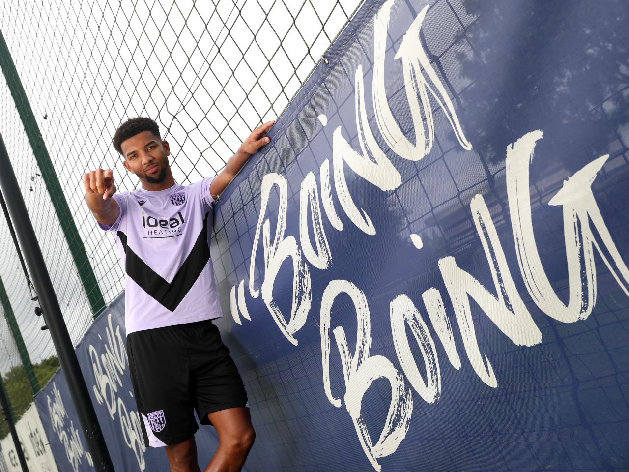 Mason Holgate stood in the home shirt next to a sign which says Boing Boing pointing and smiling at the camera  