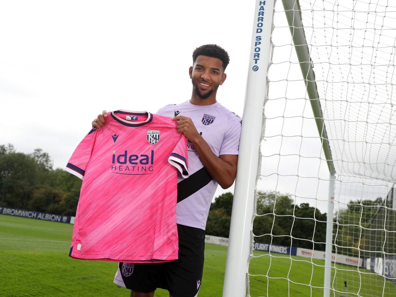 Mason Holgate smiling at the camera holding up a pink away shirt 