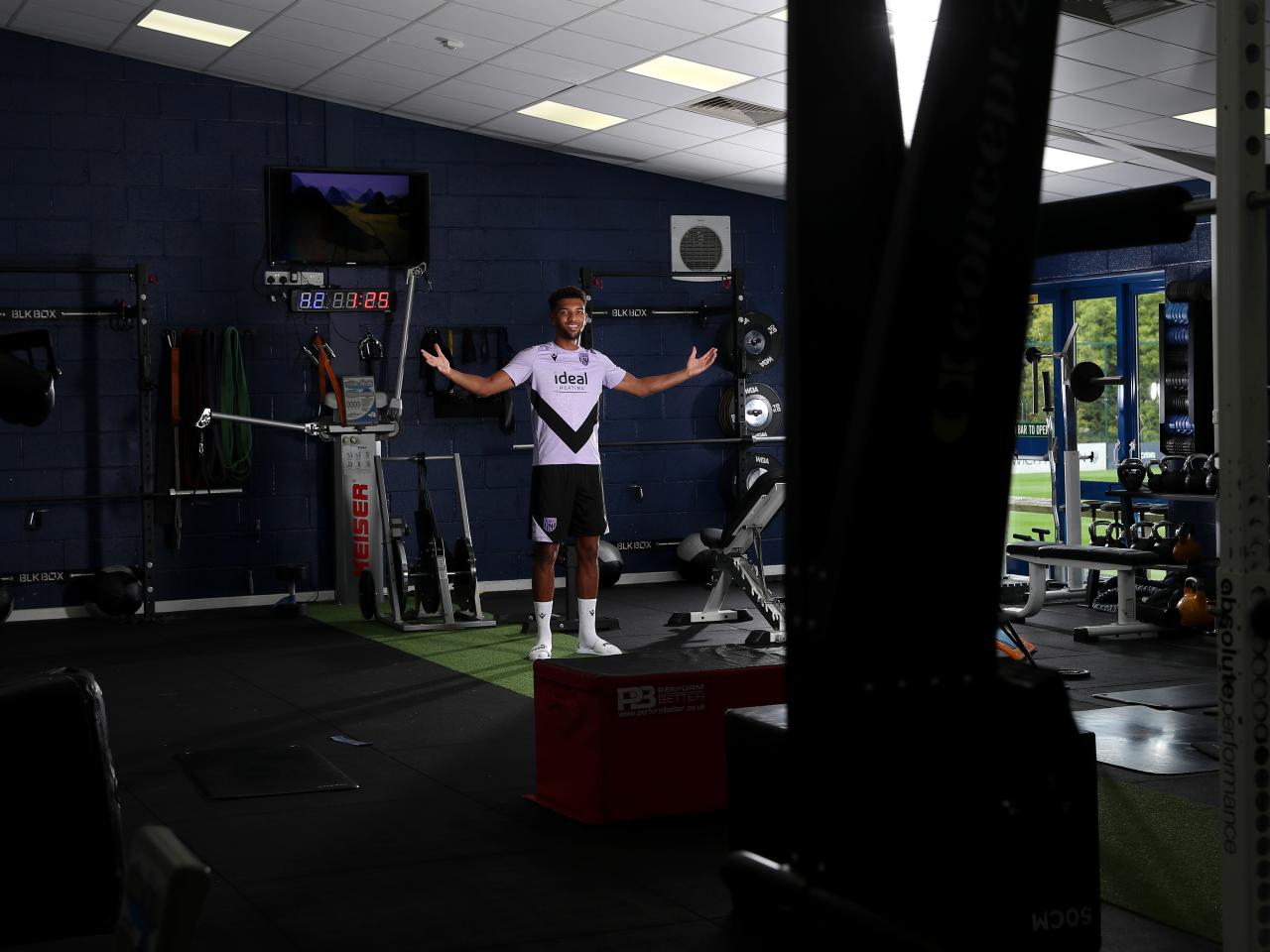 Mason Holgate smiling at the camera and holding his arms out while stood in the gym