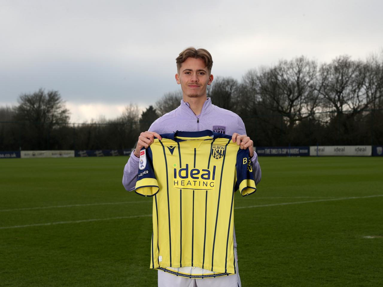 Isaac Price holding up a WBA yellow away shirt 