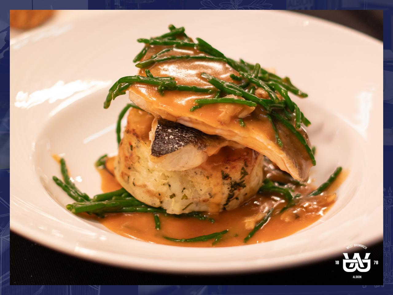 A plate of fish served on top of potatoes with samphire