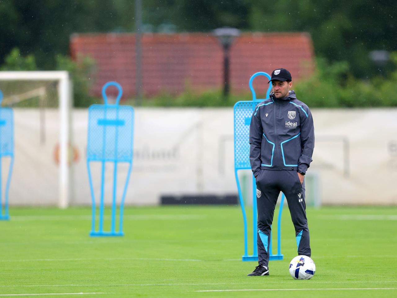 Ryan Mason watching training in the rain stood next to a mannequin in a cap