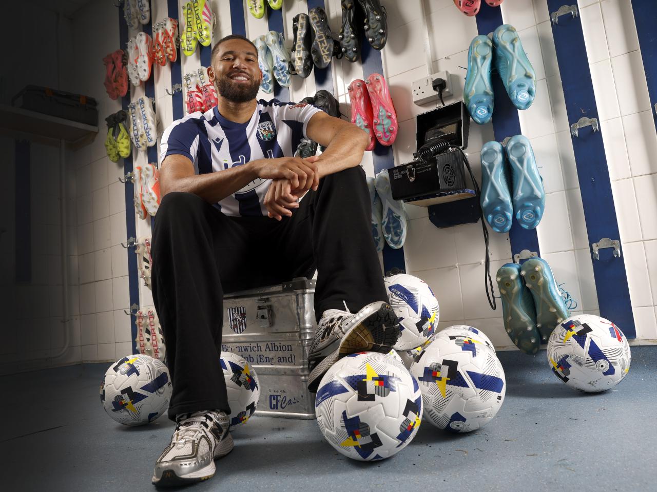 George Campbell sat in the boot room in a home WBA shirt smiling at the camera with a ball under his foot