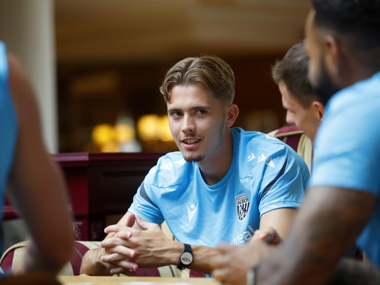 Isaac Price looking at his team-mates while playing cards