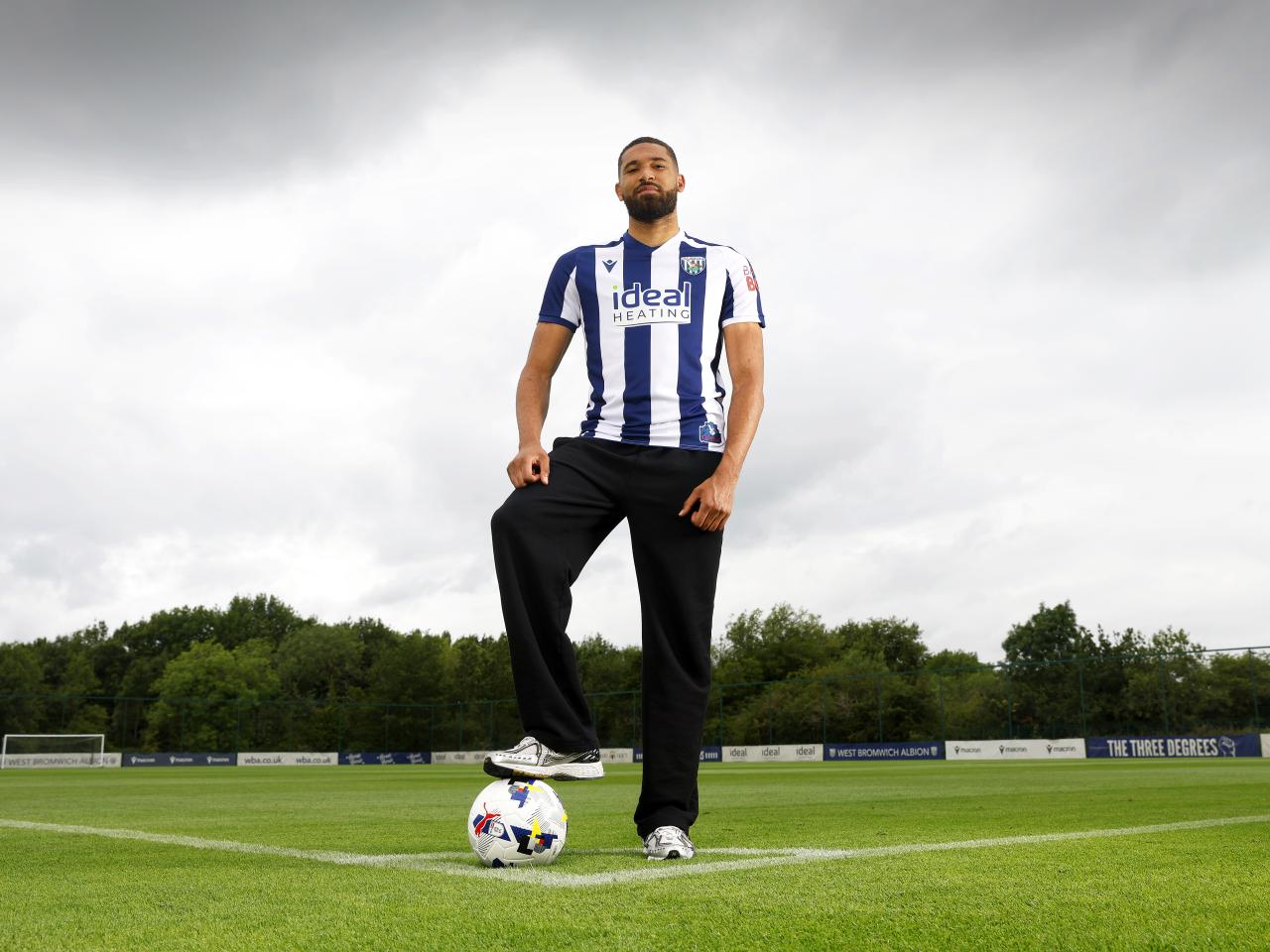 George Campbell stood on a training pitch with his foot on a ball with a home shirt on smiling at the camera 