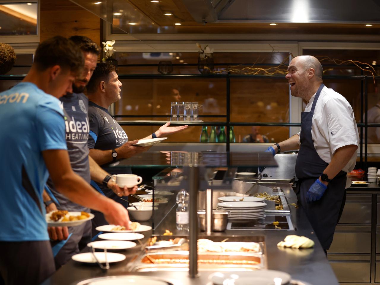 A WBA chef laughing with players and staff in the kitchen at the hotel