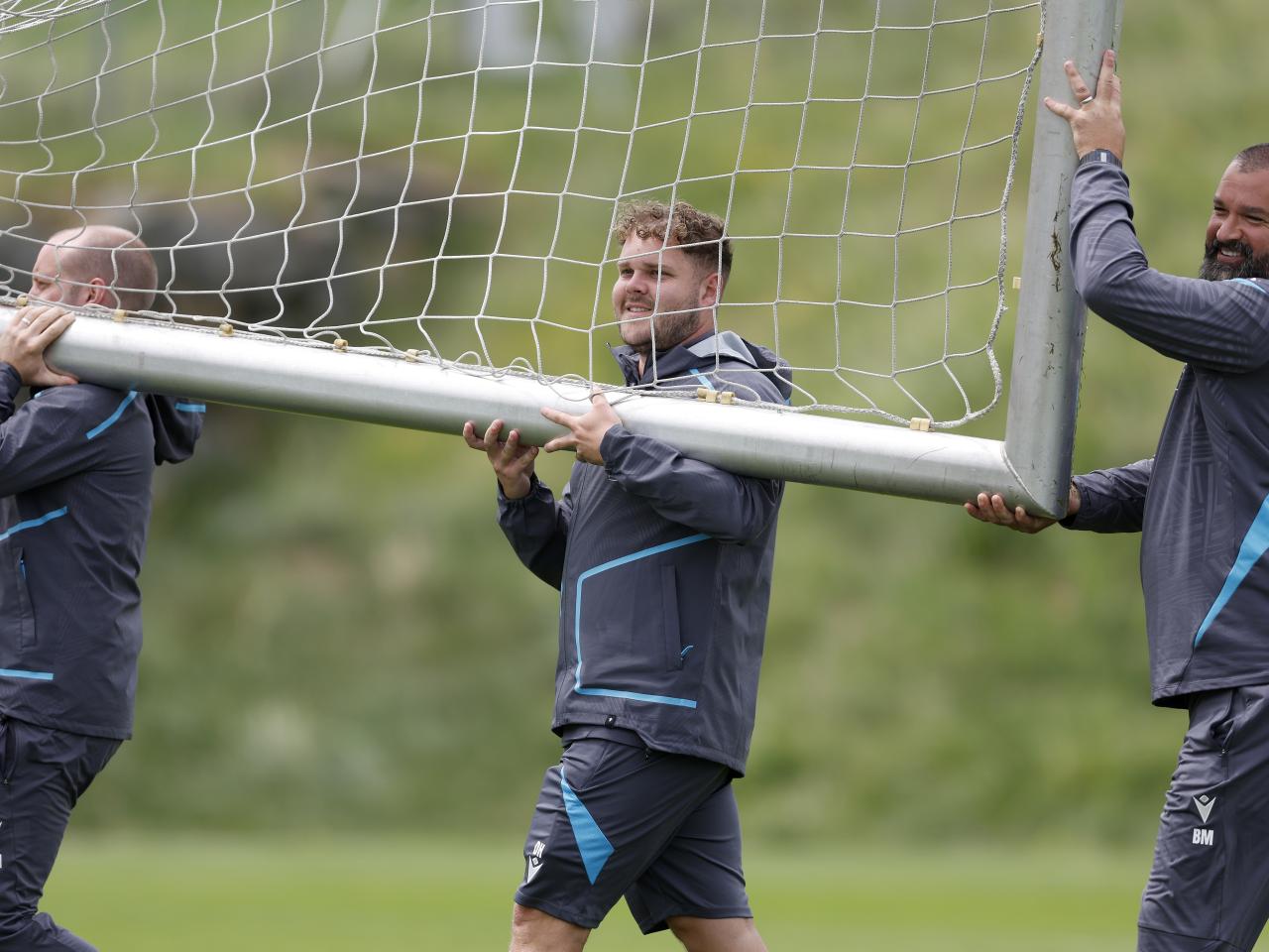 Three Albion staff members carrying a goal on a training pitch 