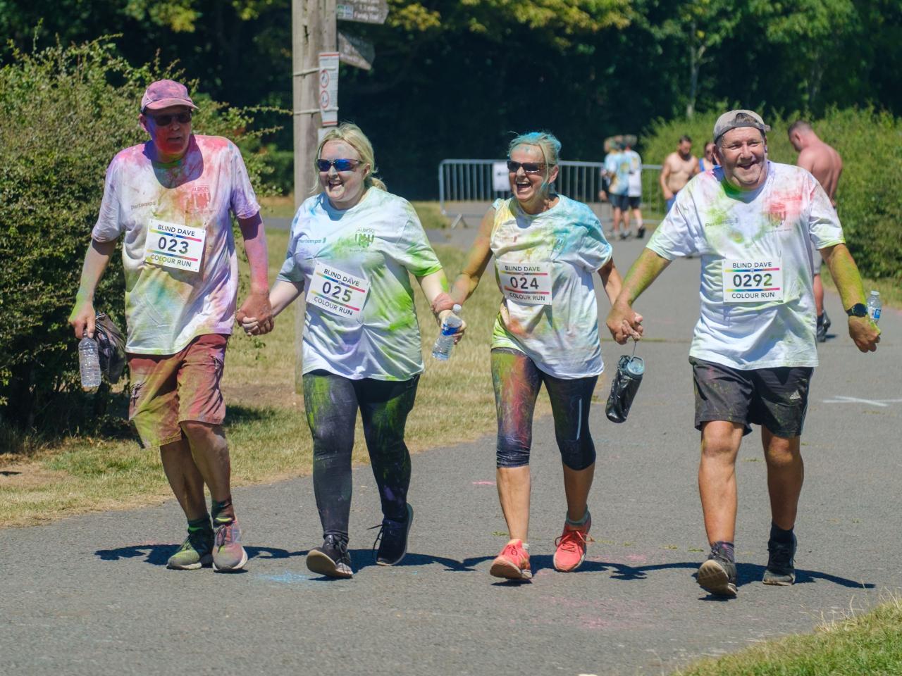 Four adult participants holding hands heading towards the finish line.