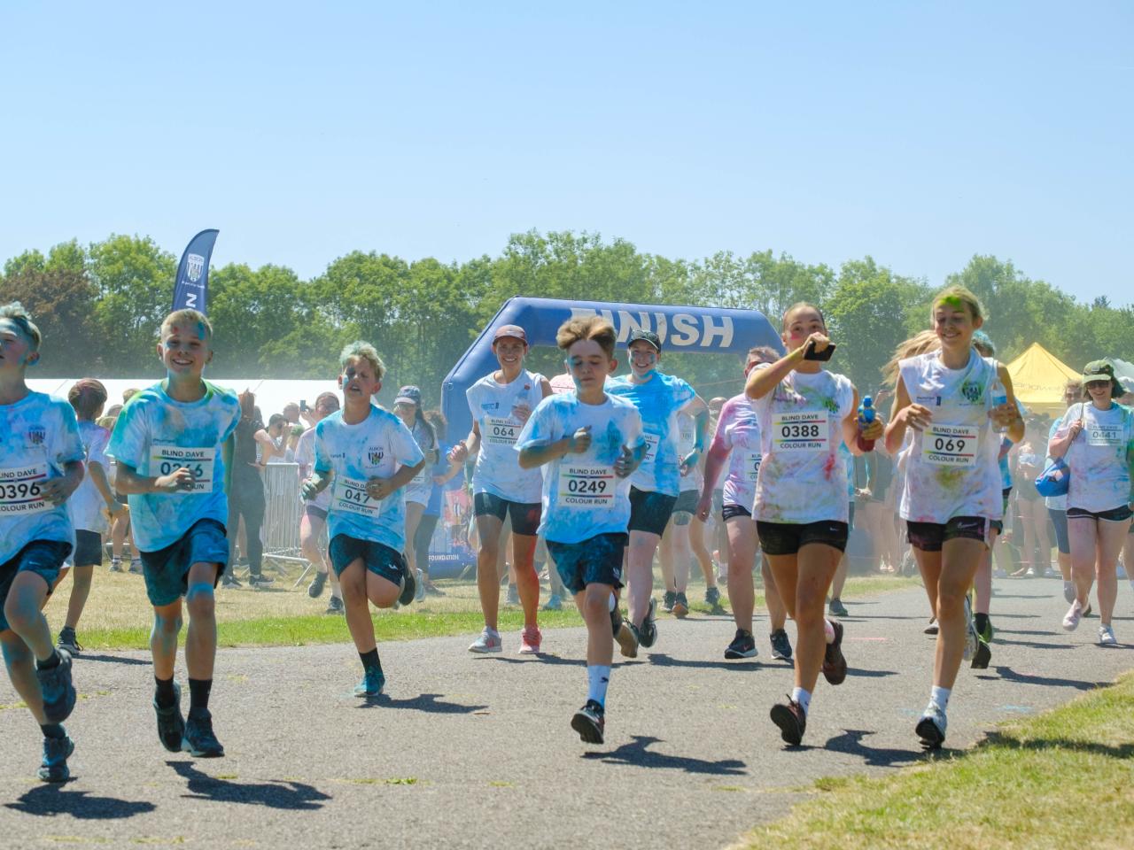 Large group of second wave runners, covered in paint, leaving the start line.