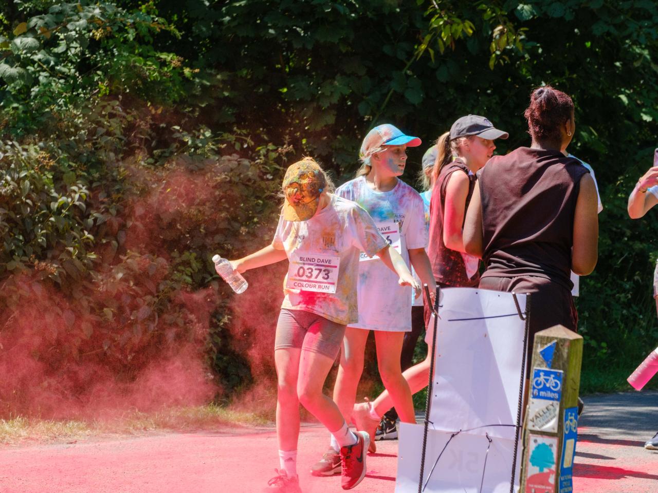 Runners passing colour station being douse with red powder.
