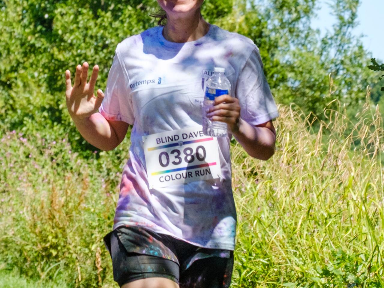 MP Sarah Coombe, waving and holding a bottle of water, as she running pass the pond.