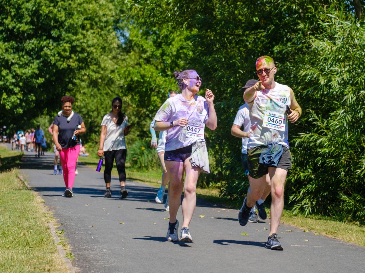 Man and woman running along the path. Woman is laughing while man is pointing at the camera.