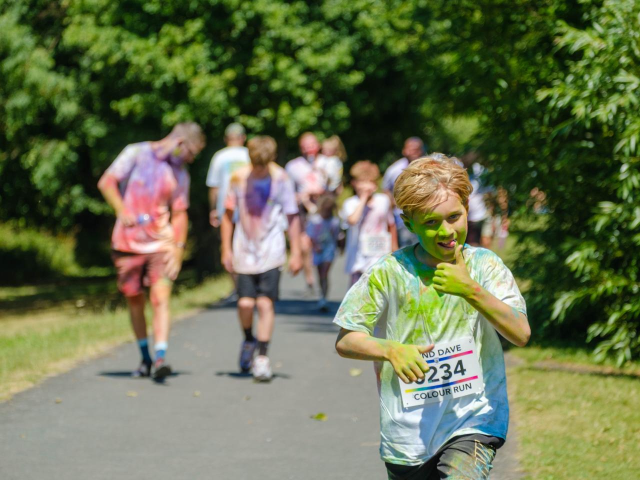 Young runner gives the thumbs up and tongue out, with group of runners in the background.