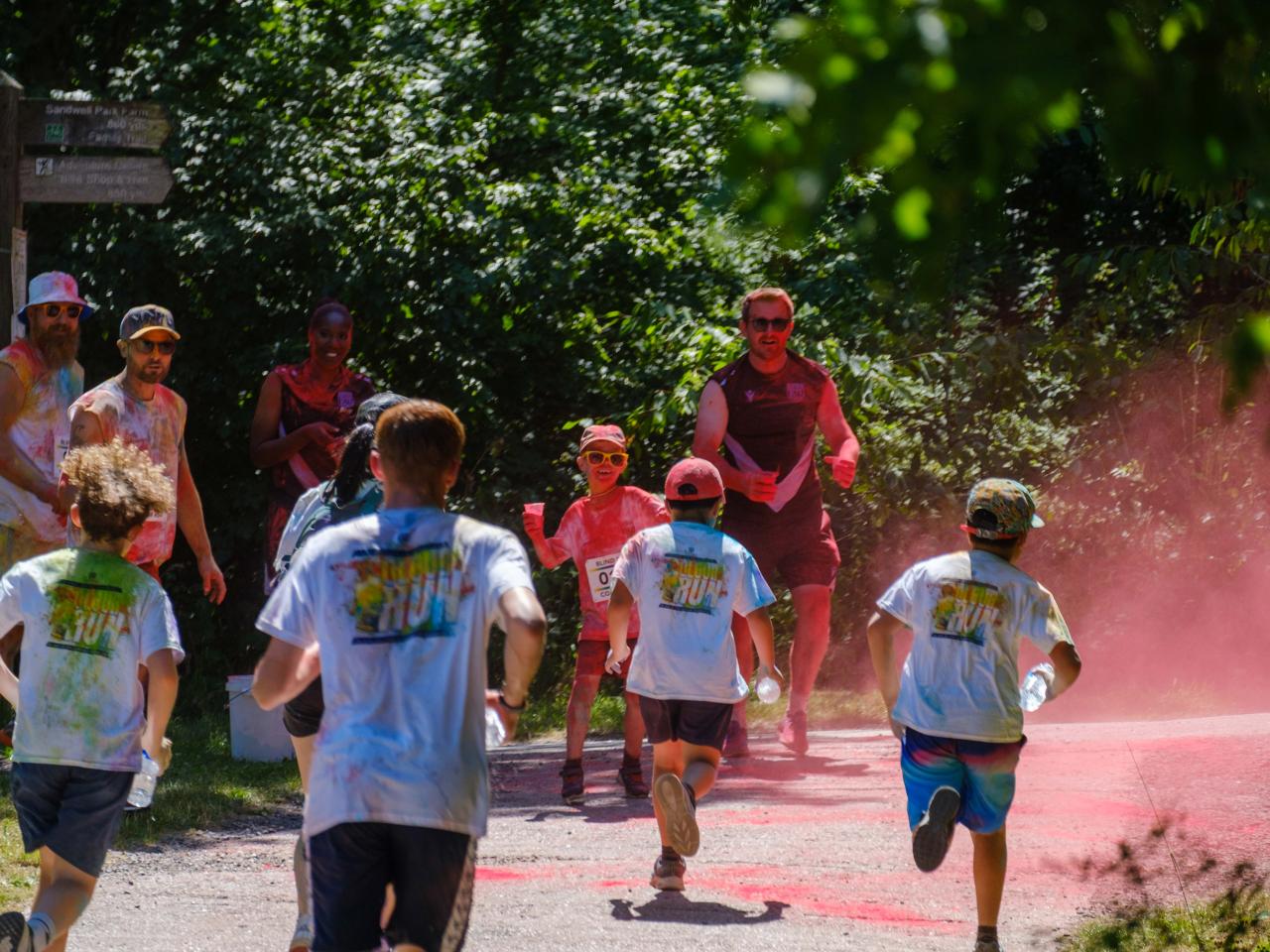 Group of five runners, heading towards a mist of red, with Foundation staff and volunteers waiting to douse them with paint.