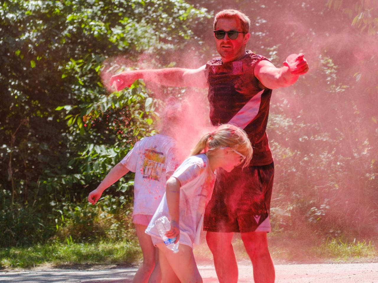 Young runners running under the arms of Foundation staff as he releases red paint.
