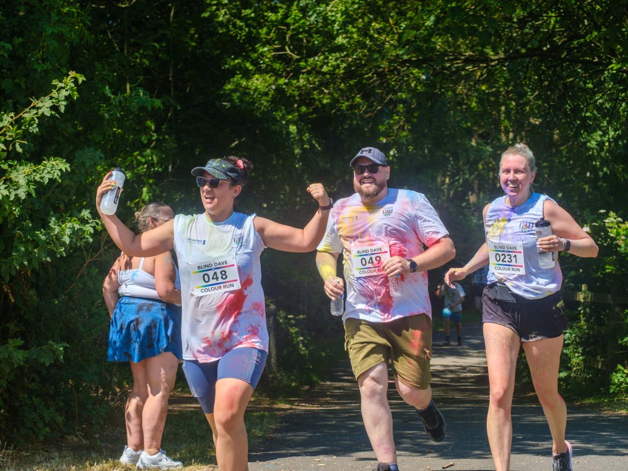 Three runners holding water bottles, 048 flexing her muscles, heading towards the final stretch.