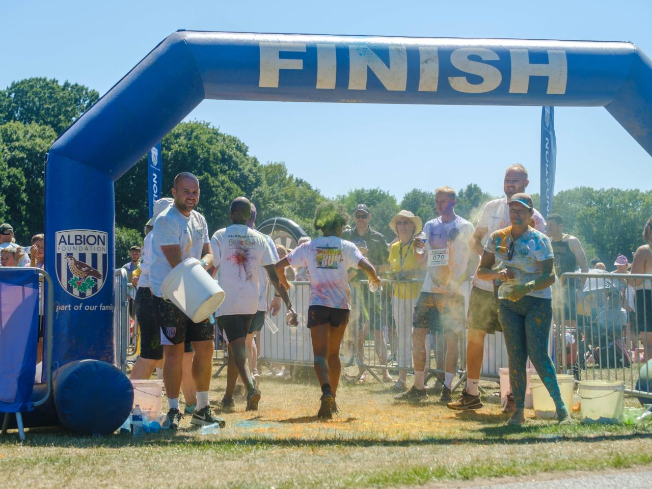 Runners crossing the finish line, as staff and volunteers throw paint.