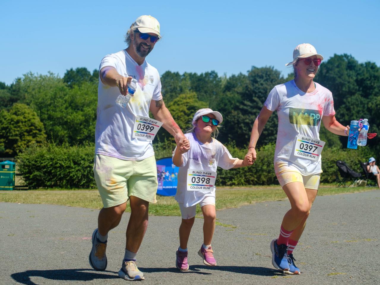 Parents and child holding hands running towards the finish, father pointing at the camera. 