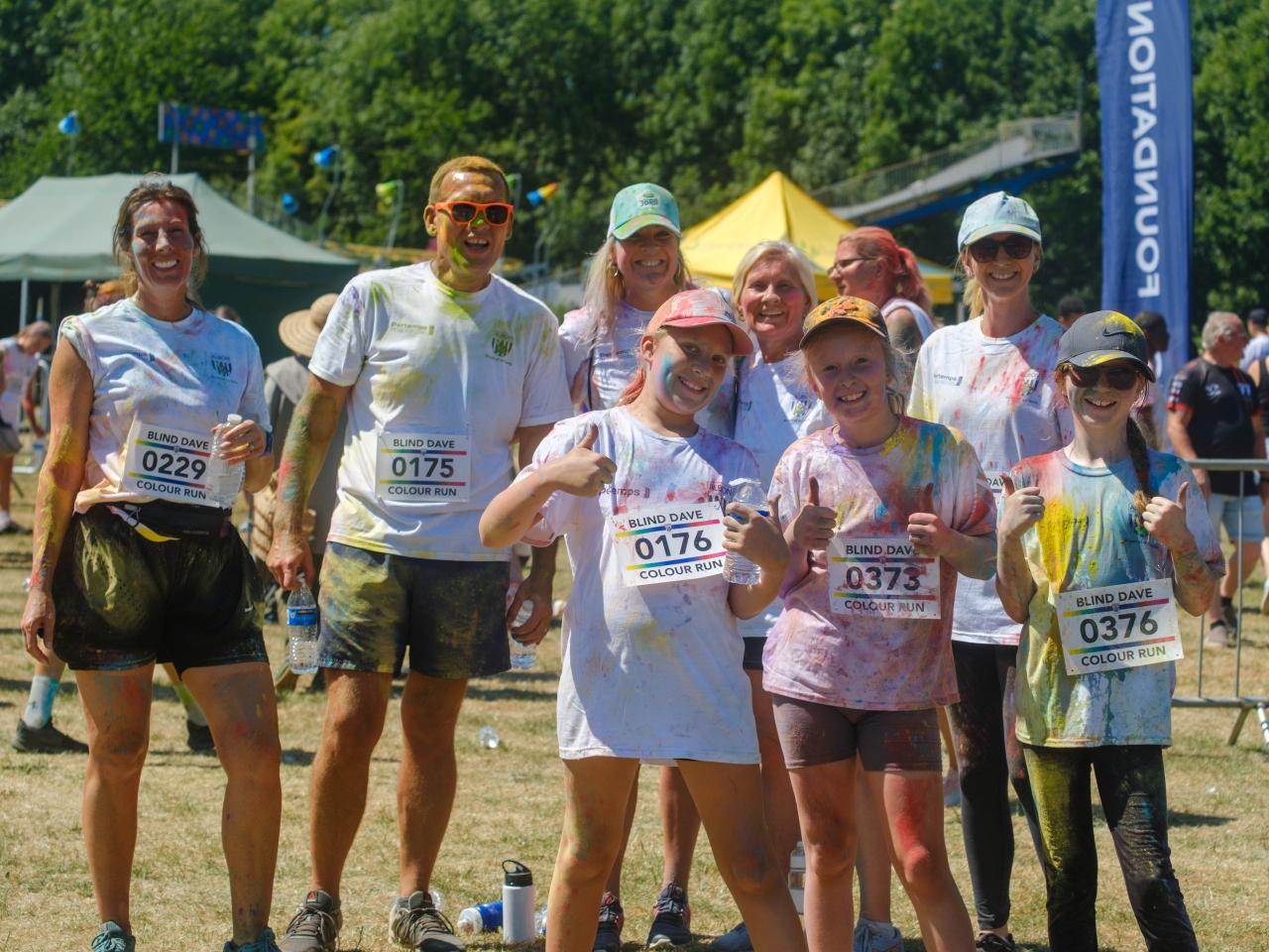 Mixture group adults and children smiling and thumbs up after completing the Colour Run.