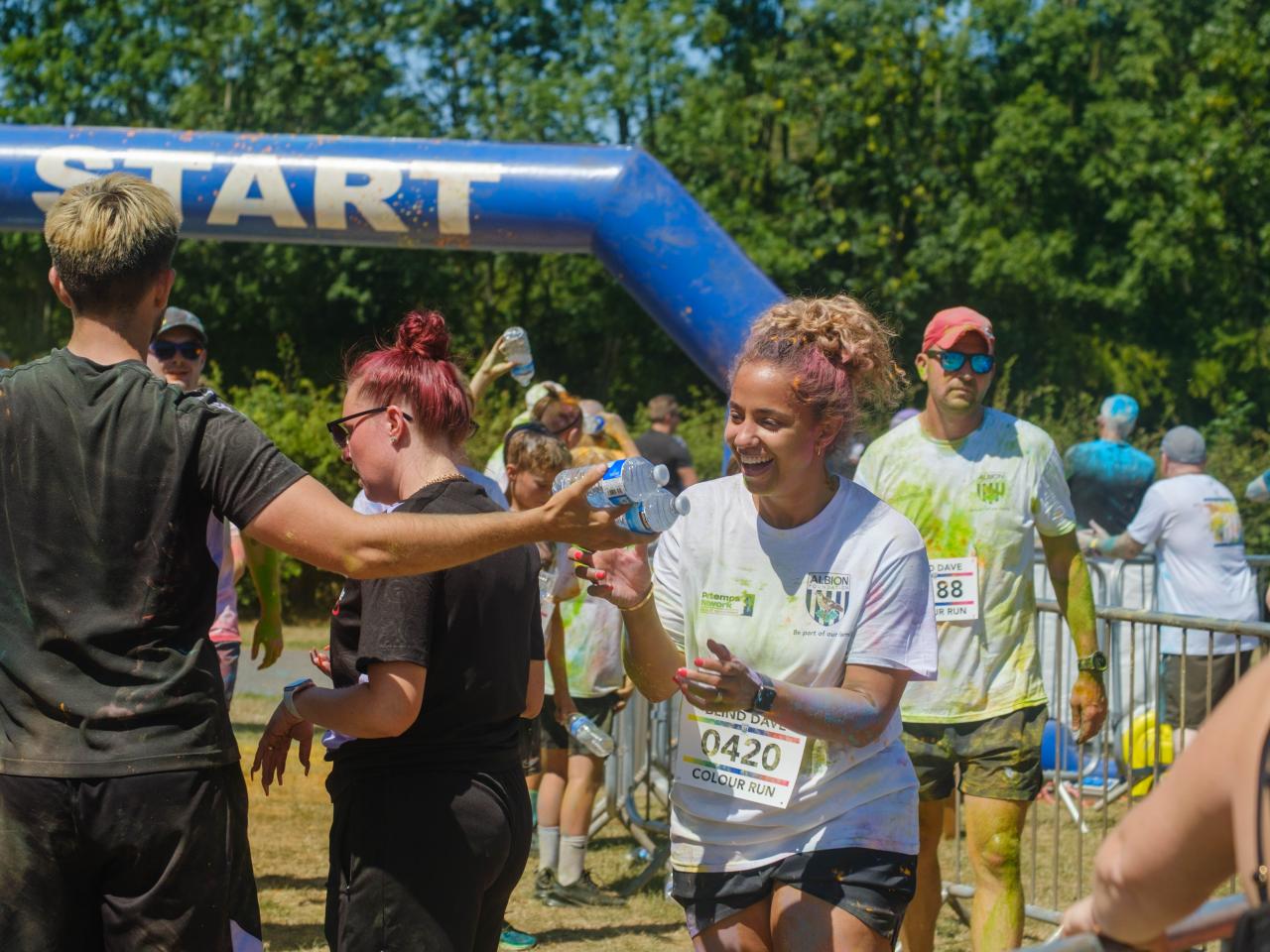 Runner 0420 smiling, as she is handed a bottle of water from Foundation staff at the end of the run.